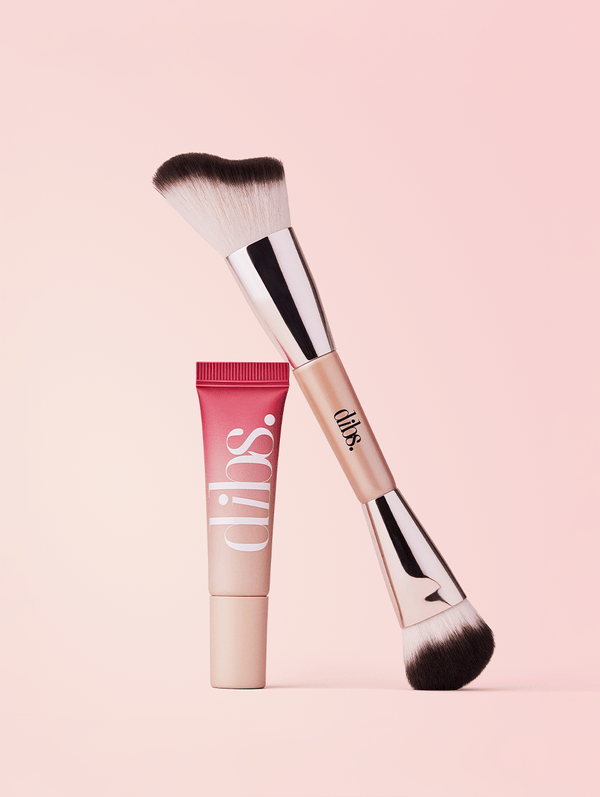 Makeup brush and liquid blush tube with 'dibs' branding on a pink background