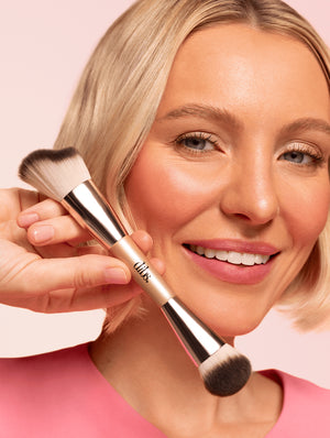 Woman holding a makeup brush against a pink background
