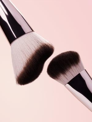 Two sides of makeup brush with black bristles on a pink background