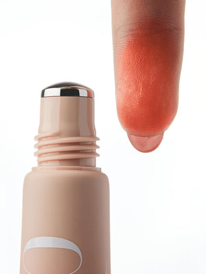 Cool Blush roller applicator with a swatch of orange color on a finger against a white background