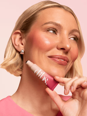 Woman holding a pink liquid blush to her facewith 'dibs' branding against a light pink background