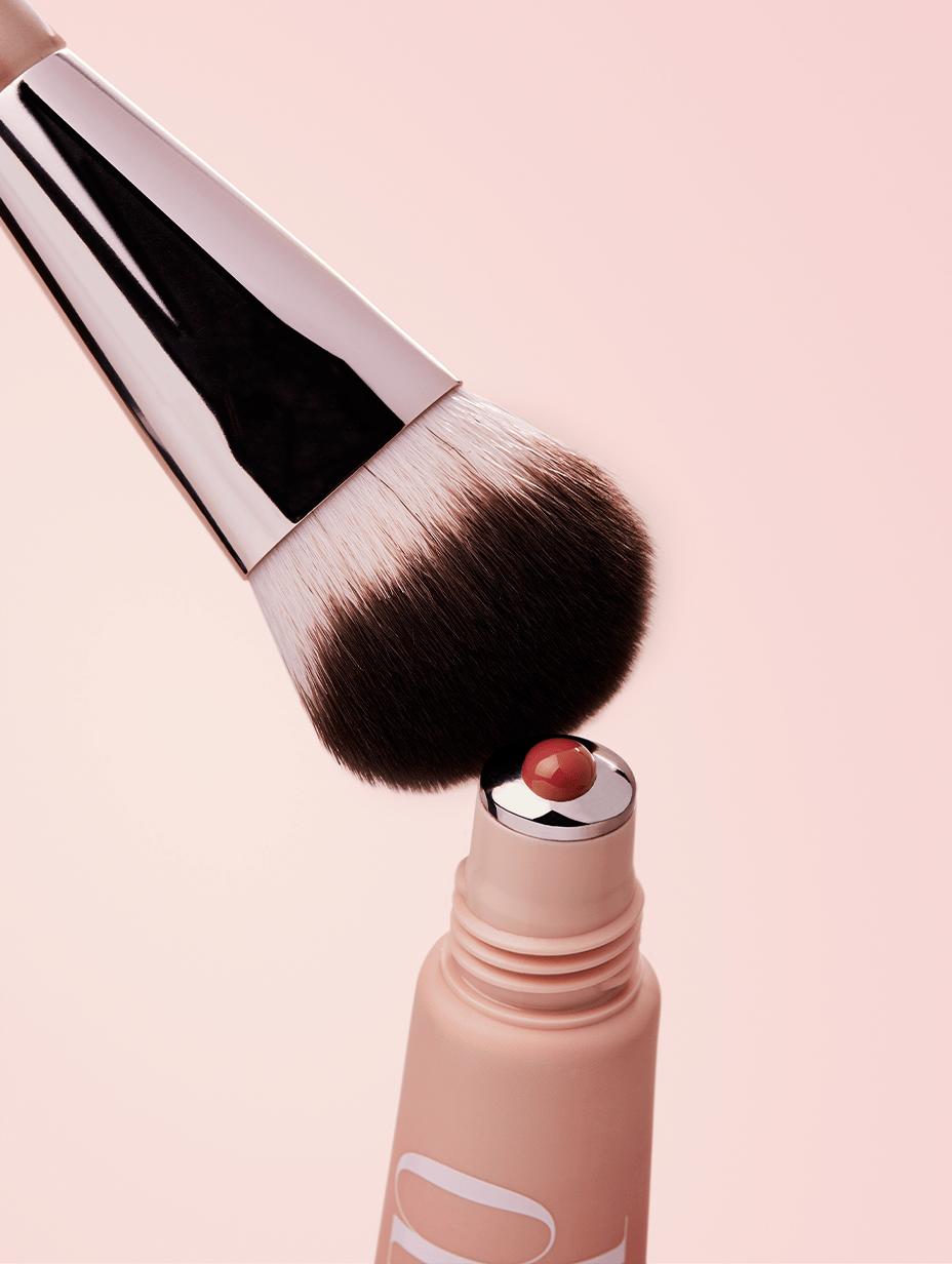 Makeup brush with liquid blush coming out of applicator on a light pink background