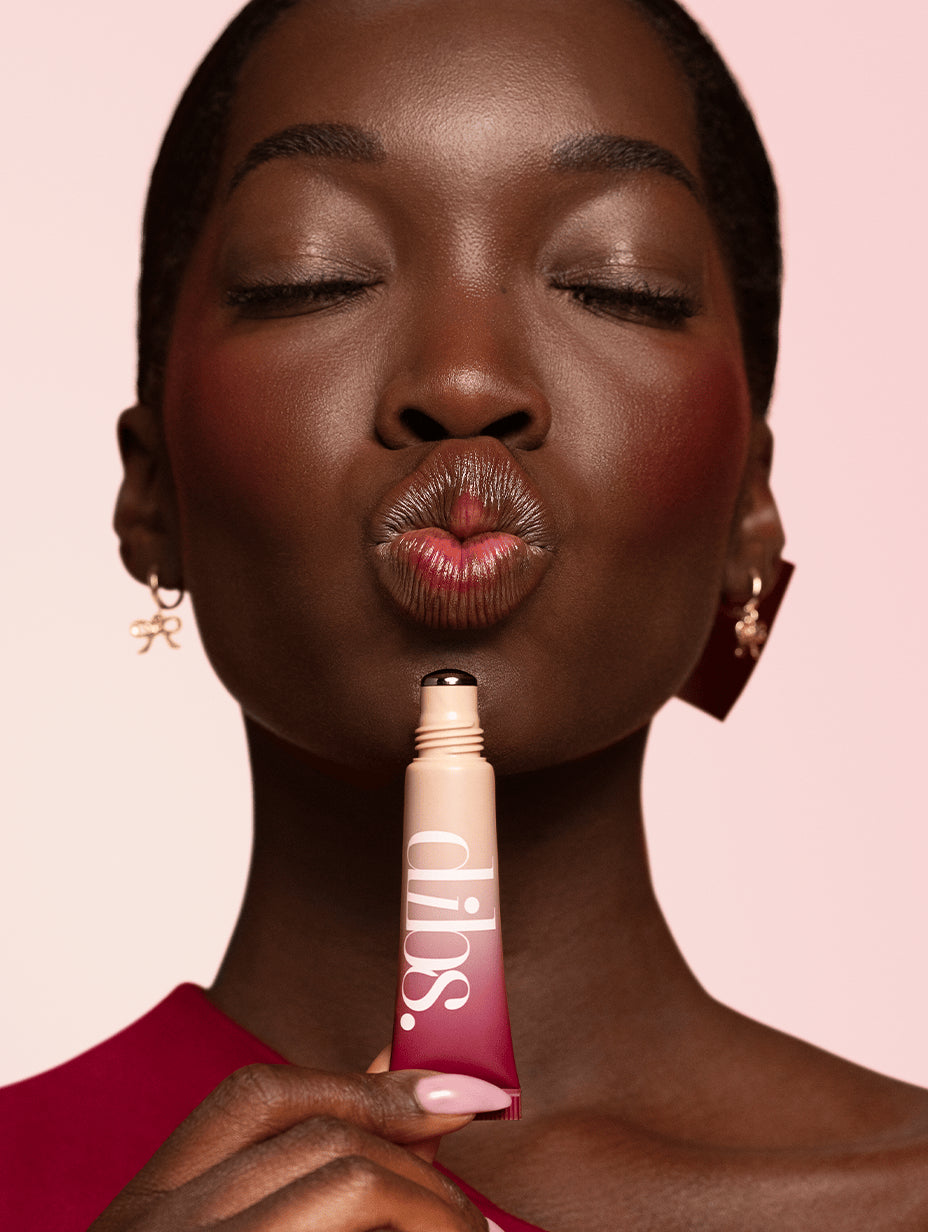 Woman holding a Cool Blush Cheek Stain tube with 'dibs' branding against a pink background