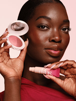 Woman holding a pink baked blush and liquid blush tube with a visible brand logo against a pink background