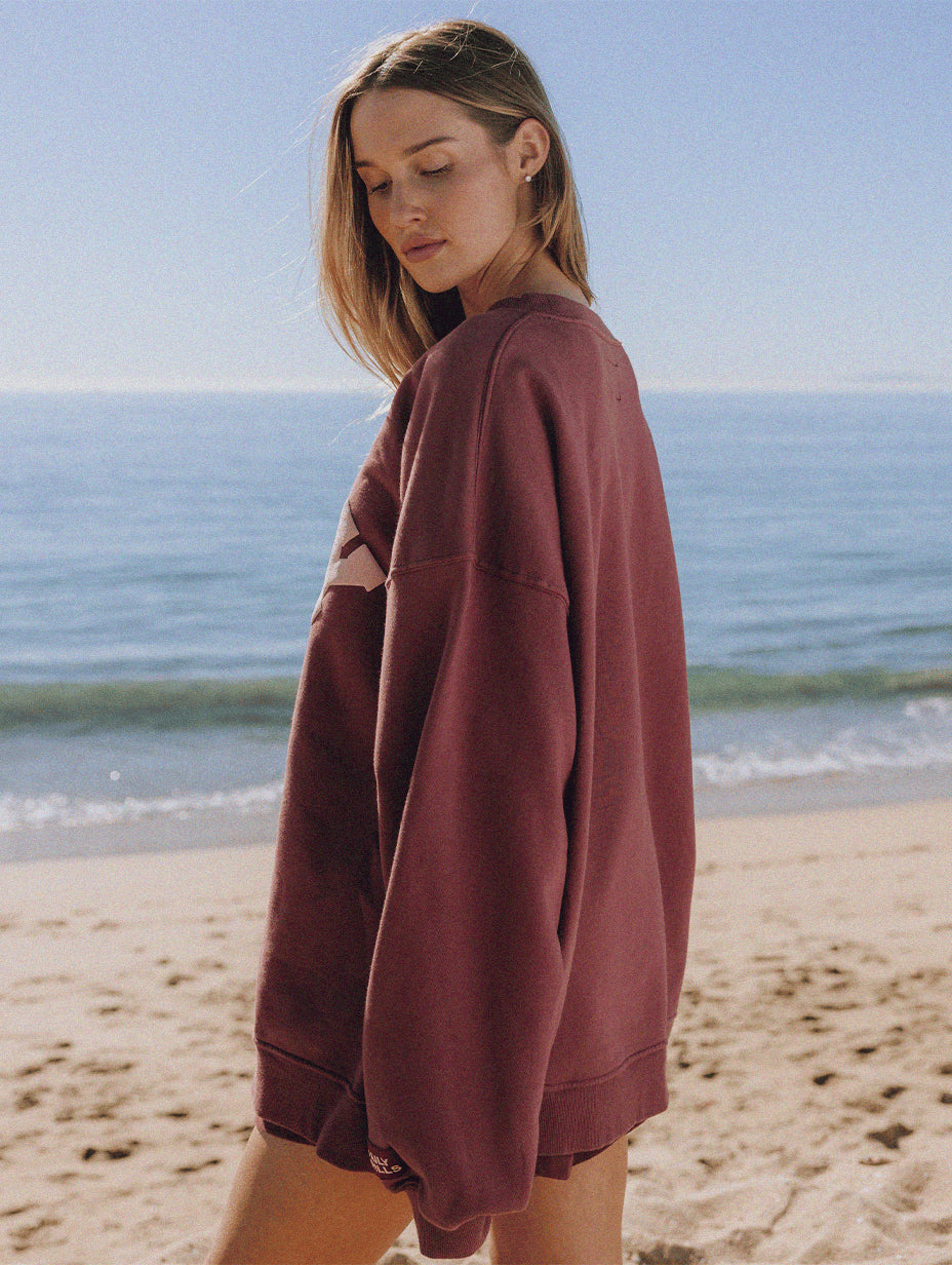 Woman wearing a maroon sweatshirt on a beach facing the ocean in the background